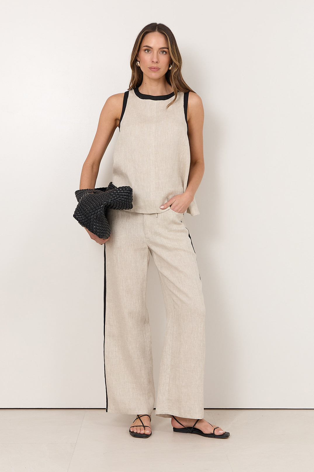 Linen pants for women featuring an elastic waistband, side pockets, and a natural straight-leg design accented with black trim. 0