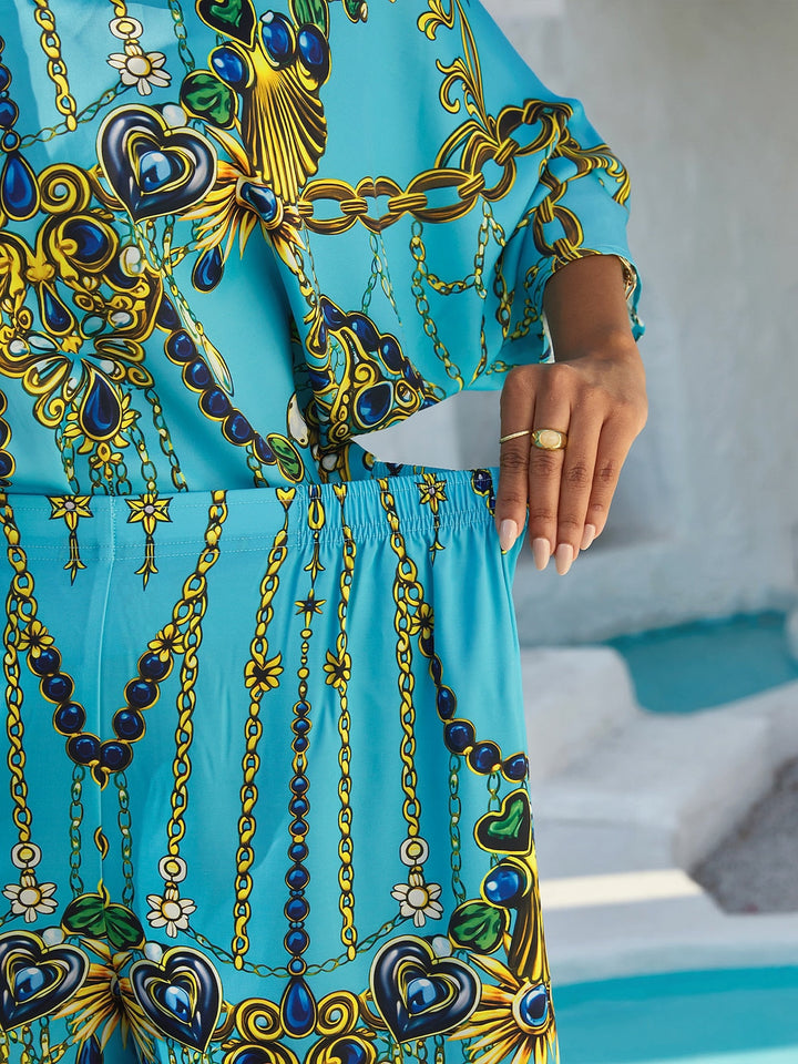 Silky satin women's pants in Mediterranean blue featuring a gold-chain print and an elastic waistband, designed in a stylish straight-leg cut. 1