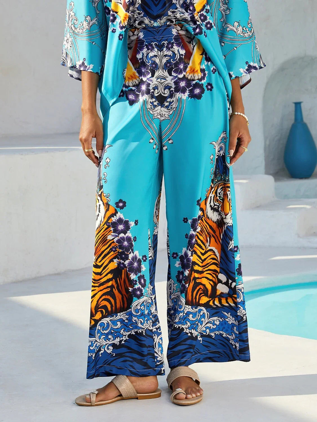 Silky satin women's pants in Mediterranean blue featuring a gold-chain print and an elastic waistband, designed in a stylish straight-leg cut. 12
