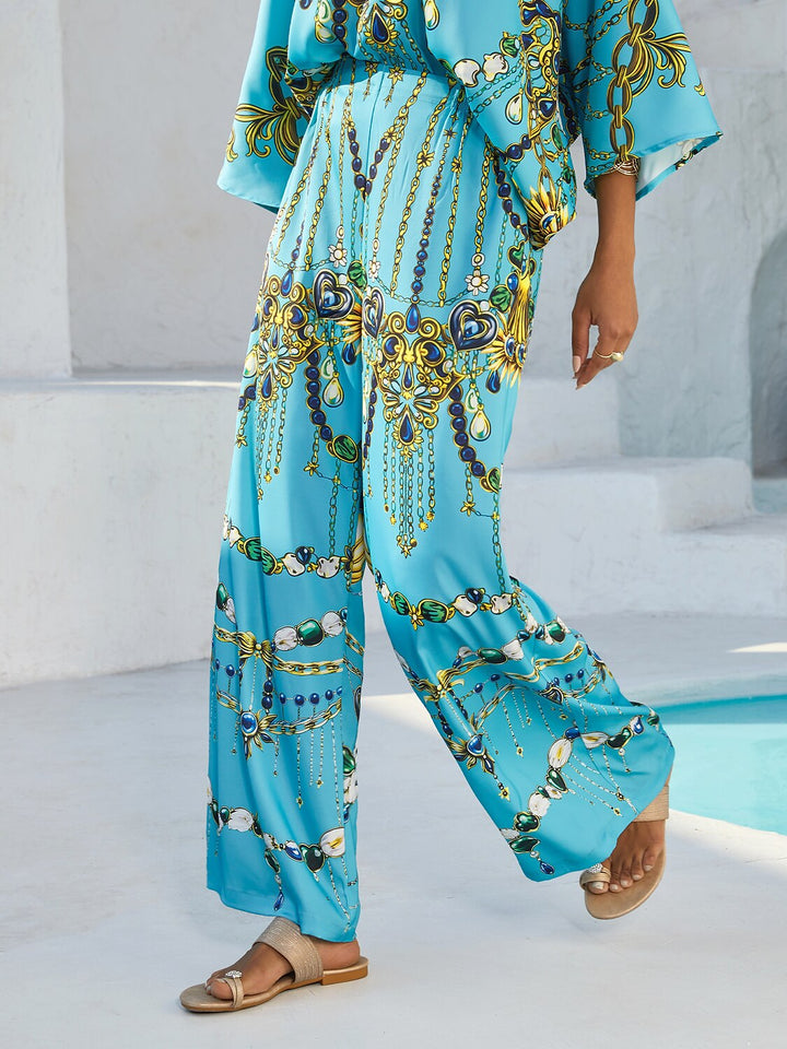Silky satin women's pants in Mediterranean blue featuring a gold-chain print and an elastic waistband, designed in a stylish straight-leg cut. 2
