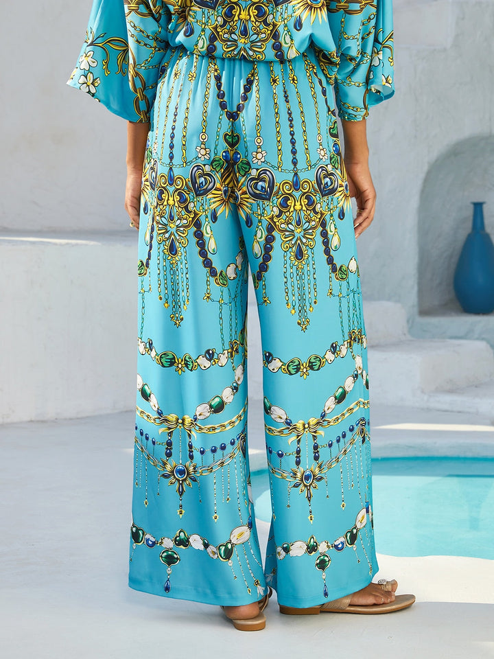 Silky satin women's pants in Mediterranean blue featuring a gold-chain print and an elastic waistband, designed in a stylish straight-leg cut. 4
